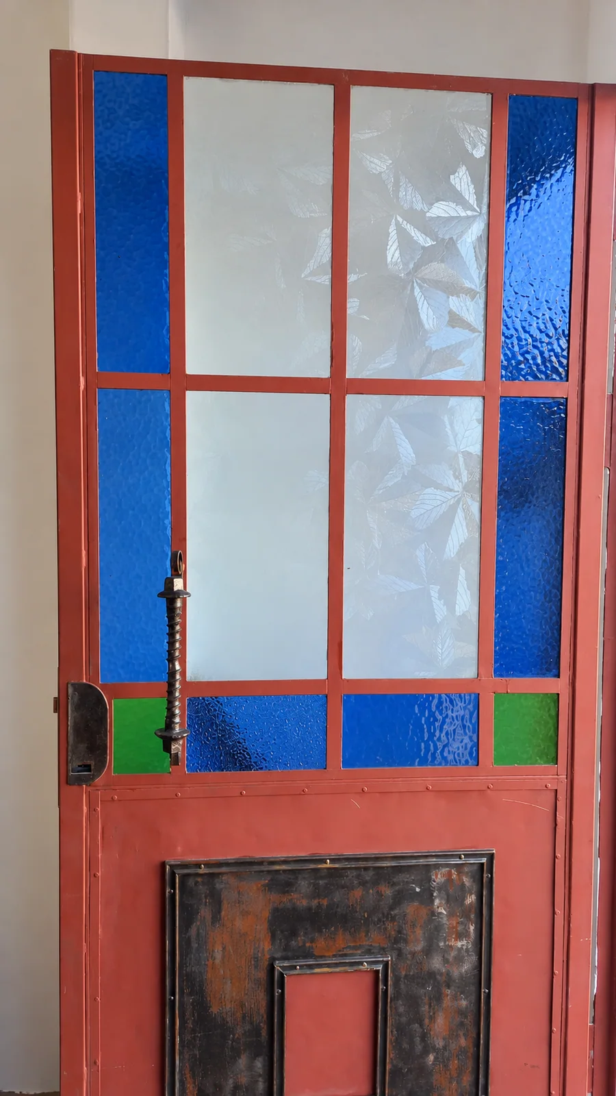 La puerta restaurada, con vidrios azules y verdes entre los paños claros.